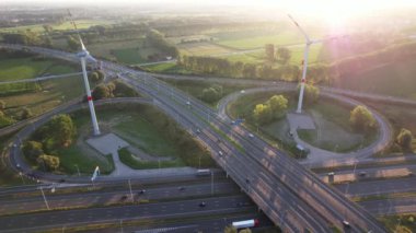 Rüzgar türbinleri günbatımında arka planda dönerken arabalar sürekli olarak otoyolda akar..