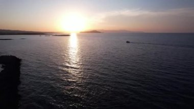 Girit, Chania 'da güneş ufkun altına batarken altın renkler suyun üzerinde dans eder. Küçük bir tekne sessizce süzülüyor, alacakaranlığın huzurlu atmosferini kucaklıyor..