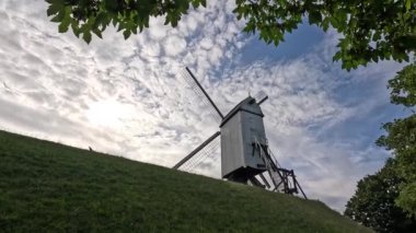 Belçika 'da manzaralı bulutların çerçevelediği akan bir nehrin yanında tarihi bir yel değirmeninin dinginliğini hissedin..