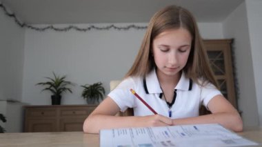 11 yaşındaki bir kız, ödevlerine dikkatle odaklanıyor. Parlak ve düzenli bir çalışma odasında yeşillik dolu bir kalemle yazıyor..