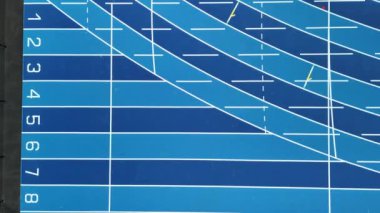 Bir atletizm stadyumunda mavi bir koşu pistinin yukarıdan çekimi. Şeritler 1-8 numaralı ve şeritleri ayıran beyaz çizgiler var..