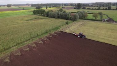 Bir traktör hasat mevsiminde aktif olarak tarlayı sürüyor, canlı kırsal araziyi ve tarım uygulamalarını gözler önüne seriyor..