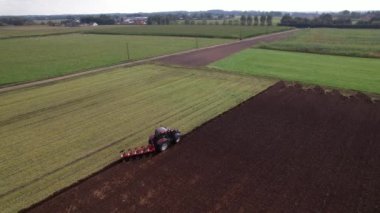 Bir traktör, güneş batmaya başladığında sakin kırsal bölgelerdeki tarlaları gayretle sürmek için çalışır..