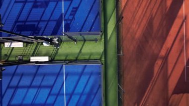 Öğleden sonra güneş ışığı, canlı tenis kortları boyunca gölgeleri vurarak göz alıcı bir görsel kontrast oluşturur..