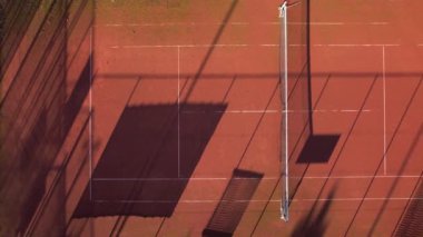 Güneş batarken gölgeler kil tenis kortuna yayılır ve sanatsal bir ışık etkileşimi yaratır..