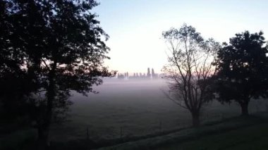 Sakin bir kırsal alan, sabahın erken saatlerinde bir alanı kaplayan sisi gösteriyor, sakin bir atmosfer yaratıyor..