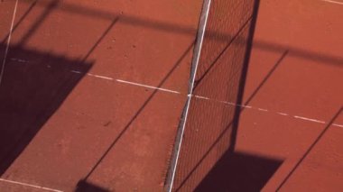 Güneş, kırmızı kil tenis kortları boyunca uzun gölgeler bırakır. Bu da sakin akşam atmosferini güçlendirir..