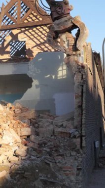 Eski bina yıkılıyor, tuğlalar ve molozlar ortaya çıkıyor. Ekipmanlar ise temiz bir gökyüzünün arka planına karşı çalışıyor..