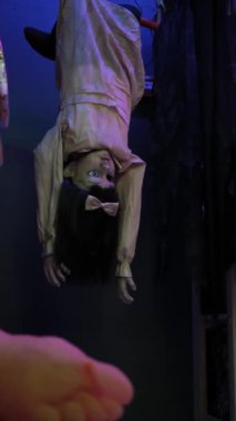 Baş aşağı duran ürkütücü bir oyuncak bebek. Ürkütücü mavi ışıkla geliştirilmiş gölgeli bir ortamda asılı duruyor.