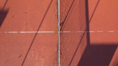 Tenis kortunun yakın plan görüntüsü gün ortası güneş ışığı altında kil yüzeyde karmaşık gölgeler bırakıyor..