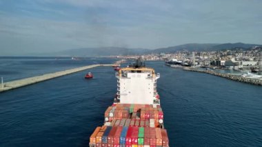 Büyük bir kargo gemisi limana yaklaşıyor. Parlak konteynırlarını manzaralı bir arka planda sergiliyor..