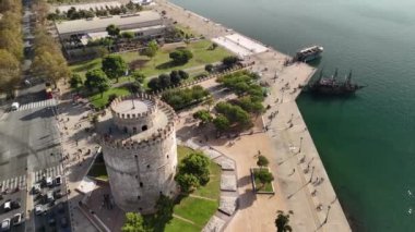 İnsanlar ünlü Beyaz Kule 'nin önünden geçerken Selanik' in canlı atmosferini hissedin. Bu ikonik konumun güzelliğini ve kültürünü keşfedin..