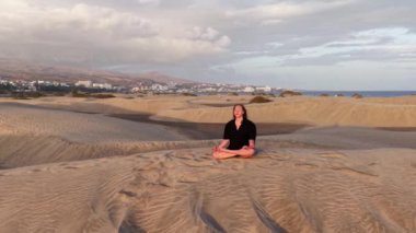 Güneş batarken, Gran Canarias kumullarının yumuşak kumlarında meditasyon yapan bir kız sakin bir atmosfer yaratıyor. Huzurlu manzara yansımasını arttırır..