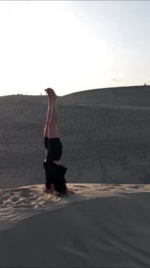 Güneş batarken Kanarya Adaları 'ndaki Gran Kanarya' nın büyüleyici kumullarında yoga pozları veren bir kız, huzurlu ve canlandırıcı bir atmosfer yaratıyor..