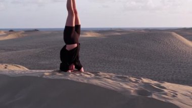 Bir kız, Gran Canaria 'nın sakin kum tepelerinde yoga pozları veriyor. Gün batımında sakin atmosferin ve nefes kesici manzaranın tadını çıkarıyor. Sahne doğanın ve farkındalığın bir karışımını yakalar..