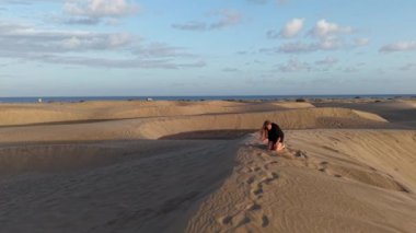 Bir kız, Gran Canaria 'nın kumlu kumullarında yogaya girişiyor, okyanusun dingin arkaplanının ve gün batımının altın tonlarının tadını çıkarıyor. Huzurlu bir ortam onun işini kolaylaştırıyor..