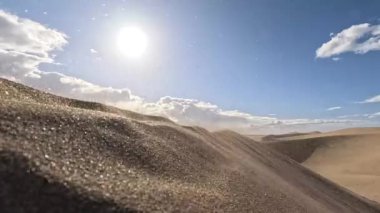 Altın kum tanecikleri, Gran Canaria 'nın vurucu çöllerinde rüzgar tarafından nazikçe süpürülür. Titreşimli güneş yukarıda parlıyor, bulutların güzel bir arkaplanını oluşturuyor..
