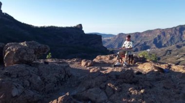 Bir müzisyen, Gran Canarias dağlarının çarpıcı zeminine karşı bir piyano setinde gösteri yapıyor. Altın saat, müziğini paylaştığı kayalık araziyi aydınlatıyor..