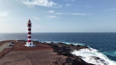 Gran Canaria 'daki güzel deniz fenerini keşfedin. Parlak kırmızı ve beyaz çizgiler, çarpan dalgaların ve engebeli uçurumların önünde dimdik durur..