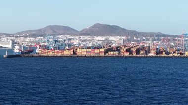 Konteyner gemileri ve kargo operasyonları Las Palmas de Gran Canaria limanında, dağların arka planına karşı hareketli bir deniz ticareti sergiliyor..