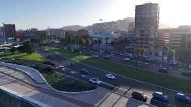 Gün batımında palmiye ağaçlarıyla kaplı ana yolda giden arabalar olarak Las Palmas de Gran Canaria 'nın hareketli atmosferini hissedin. Şehir manzarası şehir hayatını gözler önüne seriyor.