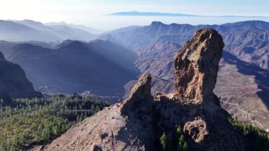 Gran Canarias 'ın çeşitli arazilerinin büyüleyici hava görüntülerini deneyimleyin, dramatik uçurumlar, yemyeşil bitki örtüsü ve ikonik kaya oluşumlarını berrak bir gökyüzü altında gösterin..
