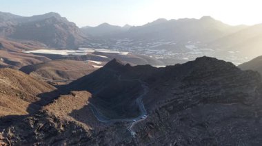 Gran Canaria 'daki Tamadaba Doğal Parkı' nın göz kamaştırıcı hava manzarasını deneyimleyin. Güneş dağlık arazide batarken, Kanarya Adaları 'nın engebeli tepelerinin doğal güzelliğini vurguluyor..