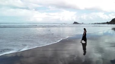 Siyah elbiseli bir kız Tenerife 'deki Benijo Plajı' nda siyah kumda geziniyor. Bulutlu bir günde dalgaları ve sakin atmosferi sever..