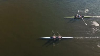 Sabahın erken saatlerinde kürekçilerin teknelerini sakin sularda süratle hareket ettirmeleri ön plana çıkıyor. Bolluk ortamları, sporcular sıkı çalıştıkça sakin atmosferi vurguluyor..