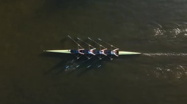 Bir grup kürekçi, sabahın erken saatlerinde yumuşak su, takım çalışması ve senkronizasyon üzerine antrenman yapıyor. Çevrenin durgunluğu etkinliğin odak noktasını artırır..