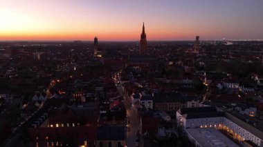 Brugge, Belçika 'nın nefes kesici hava perspektifini deneyin. Güneş şehrin üzerinde batarken. Çarpıcı ufuk çizgisinde tarihi kuleler ve akşam ışıklarıyla aydınlatılmış büyüleyici caddeler yer alıyor..