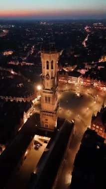 Belçika 'nın Brugge kentinin güzelliğini hissedin. Güneş batarken yukarıdan bakın. Tarihi çan kulesi, akşam aktiviteleri ve yumuşak altın ışıklarla dolup taşan büyüleyici sokakların ortasında dimdik ayakta duruyor..