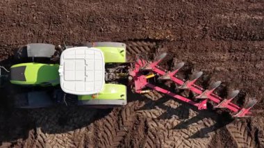 Büyük bir traktör kırsal alandaki toprağı temizlemek için bir saban kullanır. Gün ışığı, çukur açarken makineleri vurguluyor, toprağı ekin ekmeye hazırlıyor..