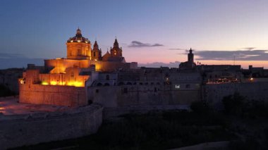 Gün batımında Mdina 'nın göz kamaştırıcı ufuk çizgisini keşfedin. Antik taş duvarlar ve görkemli binalar sıcak ışıklarla aydınlatılır ve büyülü bir atmosfer yaratır..