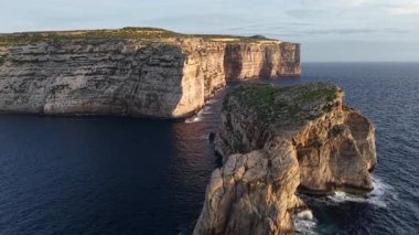 Derin mavi denizin üzerinde yükselen Maltas dramatik uçurumlarının büyüleyici hava görüntülerini deneyimleyin. Günbatımının altın ışığı bu Akdeniz mücevherinin doğal güzelliğini arttırır..