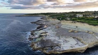 Güneş batarken engebeli arazi ve sakin suların sergilendiği, manzara ve adaların üzerine sıcak bir parıltı saçan Malta 'nın büyüleyici sahil kayalıklarına tanık olun..