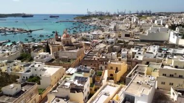 Malta 'nın ilginç bir balıkçı kasabası olan Marsaxlokk' un nefes kesici hava perspektifine hayret ediyorum. Turkuaz sularda sallanan renkli tekneleri resmedilmiş kıyı manzarasına karşı sergiliyor..