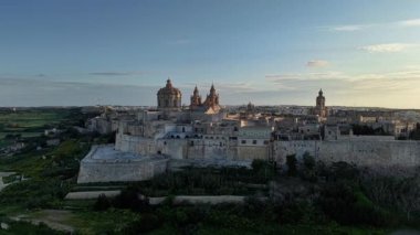 Mdina, Maltas antik kale şehrinin çarpıcı hava manzarasını tecrübe edin. Güneş, taş duvarların ve gotik yapıların güzelliğini ortaya çıkaran tarihi mimarinin üzerine batıyor..