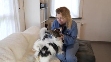 Bir kadın rahat bir kanepede rahatlar, parlak bir oturma odasında iki köpeğiyle şakalaşır. Evcil hayvanlar onu sevgiye boğarken kahkaha havayı dolduruyor..