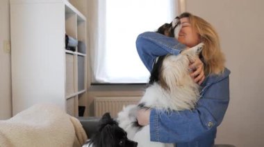 Parlak ve misafirperver bir oturma odasında bir kadın, iki mutlu köpeğiyle etkileşime girdiğinde neşeli bir etkileşim oluşur. Neşeli enerji boşluğu dolduruyor, sevgiyi ve arkadaşlığı gösteriyor..