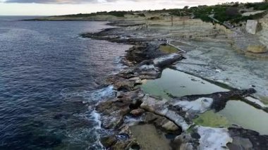 Karmaşık kaya oluşumlarının sakin sularla buluştuğu büyüleyici Malta kıyı şeridinin üzerinden uç. Gün batımının altın renklerine bakın kayalık havuzlara yansıyarak büyüleyici bir manzara yaratıyor..