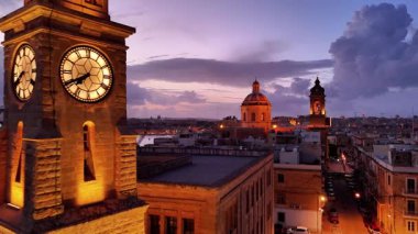 Gün batımında Malta Valletta 'nın nefes kesici hava manzarasına tanık olun. Video, şehrin ikonik saat kulesini, güzel kubbeleri ve sıcak akşam ışıklarıyla aydınlatılmış büyüleyici caddeleri yakalıyor..