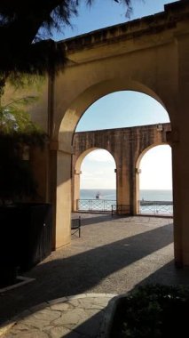 Malta 'nın Valletta kentinin bahçe terasında ziyaretçiler tarihi kemerlerin çerçevelediği güzel deniz manzarasının tadını çıkarabiliyorlar. Huzurlu atmosfer çevreyi rahatlatmaya ve keşfetmeye davet ediyor..