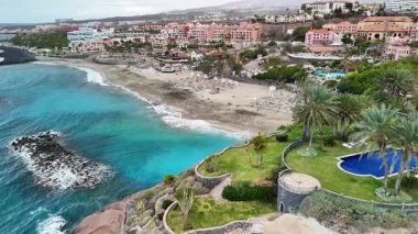 Tenerife 'nin nefes kesici sahil şeridini, sahilin manzaralı manzarasını, canlı turkuaz suyunu ve güzel palmiye ağaçlarını keşfedin. Bu konum, doğa ve rahatlığın mükemmel bir karışımını sunar..