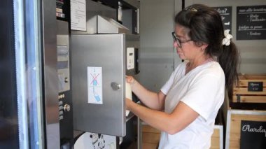 Bir kız self-servis makinesine yaklaşır ve istediği sütü seçer. O, öğleden sonra yerel bir dükkandan satın alma talimatlarını dikkatle izler..