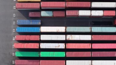Hava görüntüsü, Zeebrugge 'da renklerine göre sıralanmış çeşitli nakliye konteynırlarıyla dolu bir konteynır deposunu yakalıyor. Planda deniz lojistik ve ticaret faaliyetleri vurgulanıyor.