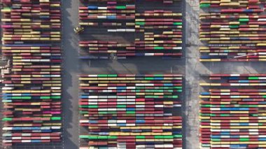 Zeebrugge limanının havadan görünüşü, düzgünce düzenlenmiş bir dizi renkli konteynır gösteriyor. Etkinlik, öğlen liman operasyonlarının verimliliğini vurgular.