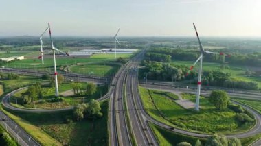 Bruges yakınlarında yemyeşil ve yel değirmenleriyle çevrili bir yol kavşağının çarpıcı hava manzarasını keşfedin. Bu güzel manzarada doğanın ve modern altyapının uyumunu deneyimleyin..