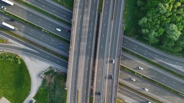 Gün ışığında yemyeşil ortamda geniş bir otoyol kavşağında birden fazla araç geziniyor. Yol yapısı çeşitli şeritler ve kesişen yollar gösteriyor..