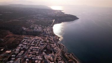 Yunanistan 'ın Girit kıyı şeridinin ufka doğru uzanmasına tanık olun. Video, altın bir güneşin altında kıyı boyunca yuva yapmış canlı beyaz yapıları yakalıyor..